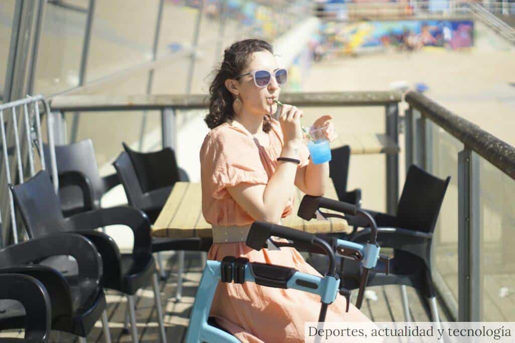 Young woman in a peach dress enjoying a refreshing drink outdoors on a sunny terrace.