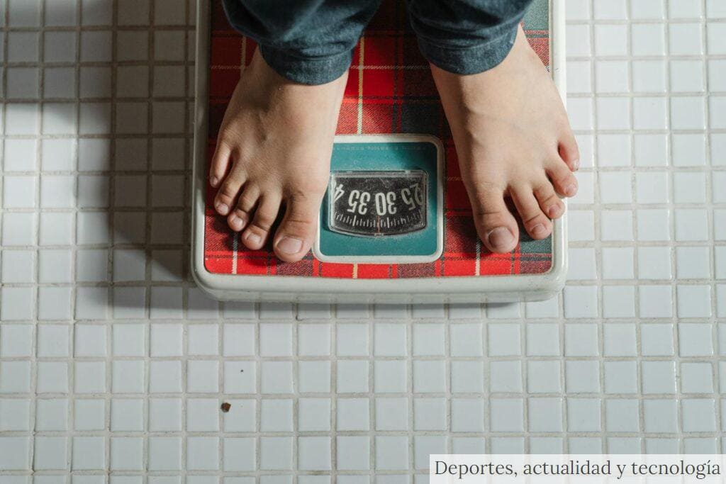 From above crop anonymous barefoot child in jeans standing on weigh scales on tiled floor of bathroom