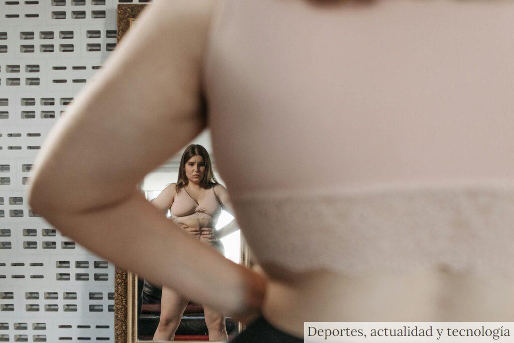 A woman examines her reflection, contemplating body image and self-perception indoors.